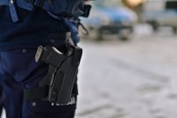widok pistoletu w kaburze na udzie policjanta, w tle policyjne radiowozy